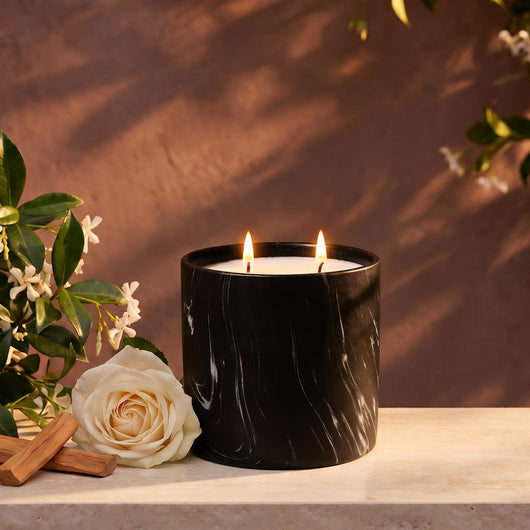 Black marble-pattern candle jar with two lit wicks and cream-colored wax