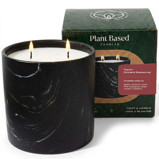 Black marbled pillar candle with lit flame next to plant-based candle box
