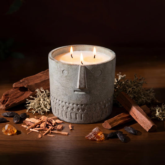 Gray stone-look face candle with three flames, set on wood with dried botanicals.