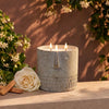 Gray stone-look face candle in round container with three lit wicks and central flame