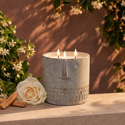 Gray stone-look face candle in round container with three lit wicks and central flame