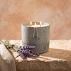 Grey stone-look candle jar with three flames, lavender sprigs beside it on linen