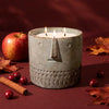 Stone-look scarecrow face candle, round gray jar with carved details and lit wicks