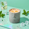 Stone-faced gray candle with three lit wicks in a textured cylindrical cup