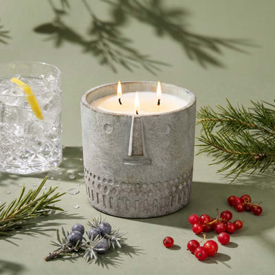 Stone-face candle, gray textured jar, three lit wicks, on tabletop
