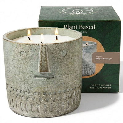 Gray stone-look face candle in jar with three flames, plant-based candles box behind.