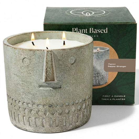 Gray stone-look face candle in jar with three flames, plant-based candles box behind.