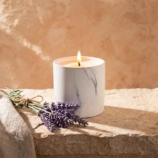 Lit white marble-style candle in a glass jar with lavender sprigs on stone